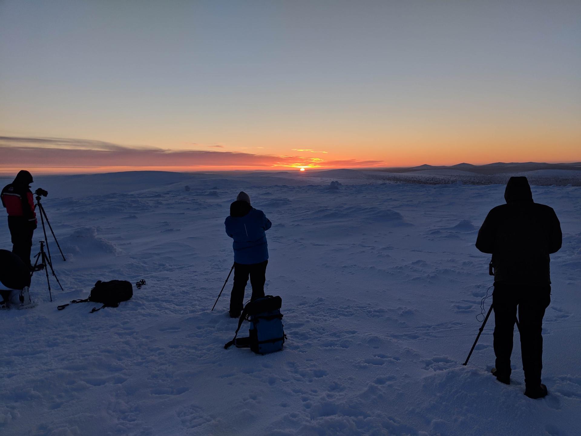 photographers on a field of snow, rising sun in background